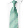 Mint-green silk necktie knotted under a white collar, with geometric floral weave and scattered rhinestones